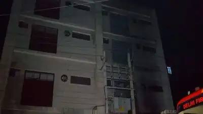 Night photo of the multi-storey shoe factory building in Mangolpuri Industrial Area, Delhi, with a Delhi Fire Service vehicle at the side after the fatal basement fire
