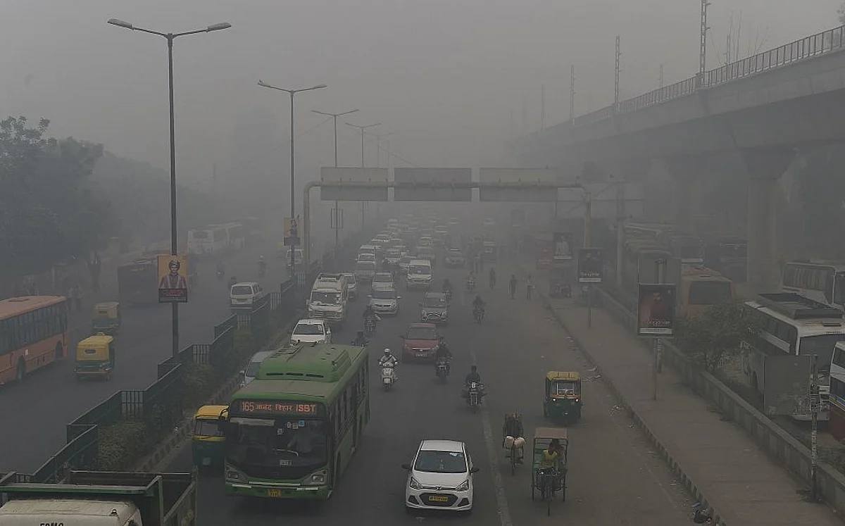 Traffic including buses, cars and auto-rickshaws moving through dense smog on a multi-lane road in Delhi