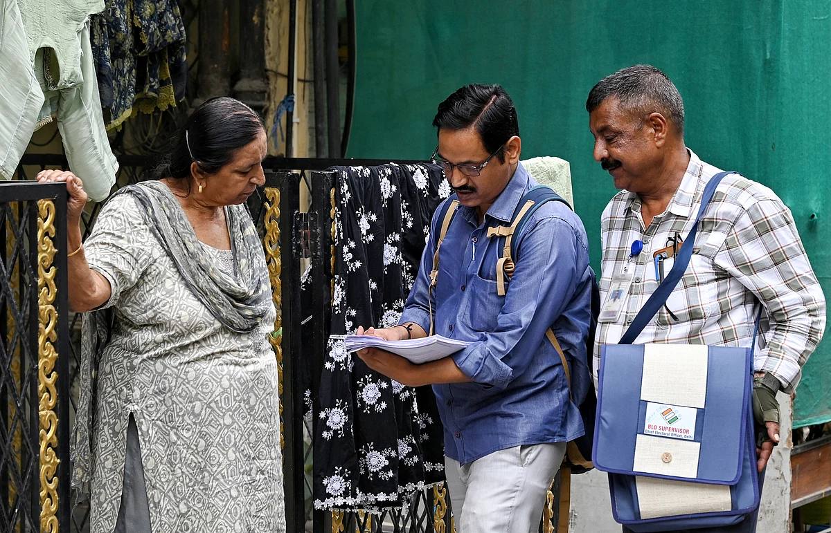 A booth-level officer with a BLO supervisor bag checks electoral roll papers with a woman resident at the gate of her Delhi home during door-to-door SIR verification