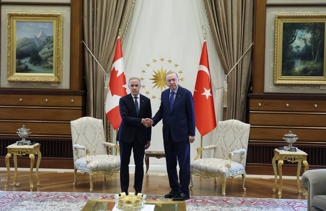 Canada's Prime Minister Mark Carney shakes hands with Turkish President Tayyip Erdogan between the Canadian and Turkish flags during their meeting in Ankara