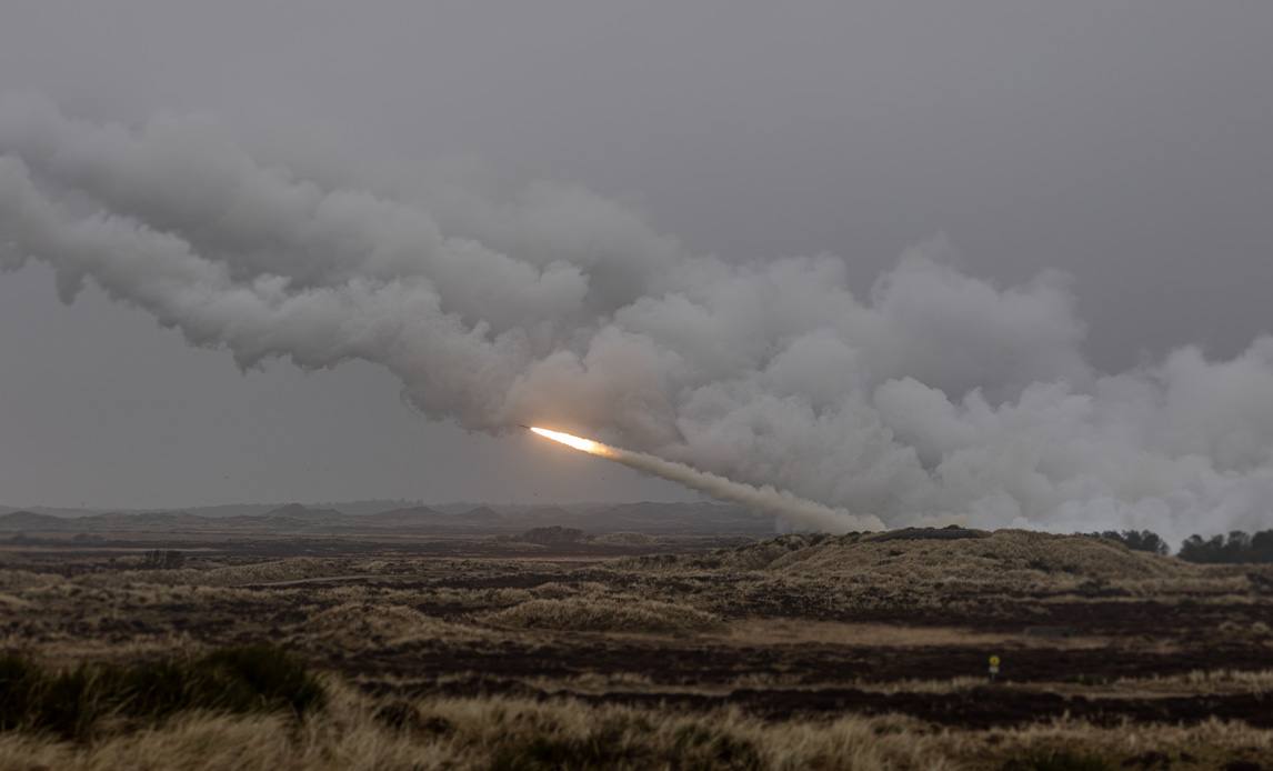 A rocket artillery round streaks across a grey sky trailing thick white smoke during a Danish Armed Forces live-fire exercise in Denmark