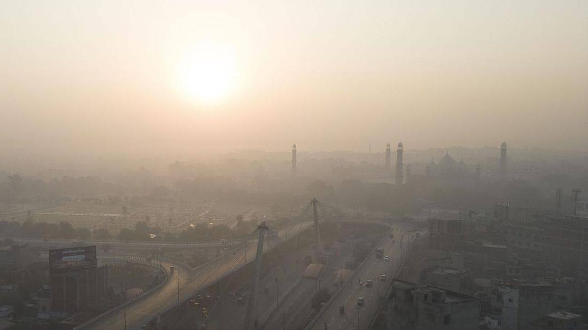 Lahore skyline and the Badshahi Mosque minarets barely visible through thick smog, with traffic moving on a flyover below