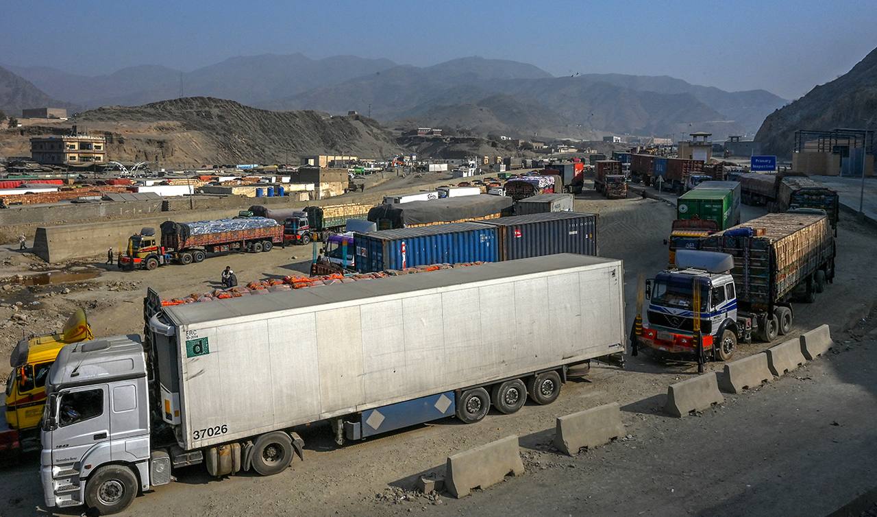 Cargo trucks and shipping containers queued at the Pakistan-Afghanistan border crossing in the Torkham area, with dry mountains behind