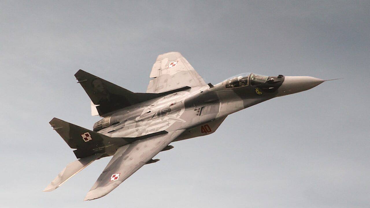 A Polish Air Force MiG-29 fighter jet in flight against a grey sky, showing Polish checkerboard markings