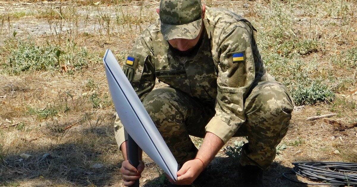 A Ukrainian soldier crouches in a field while setting up a Starlink satellite terminal — Ukraine relies on the military-grade Starshield service for drone operations and missile defence