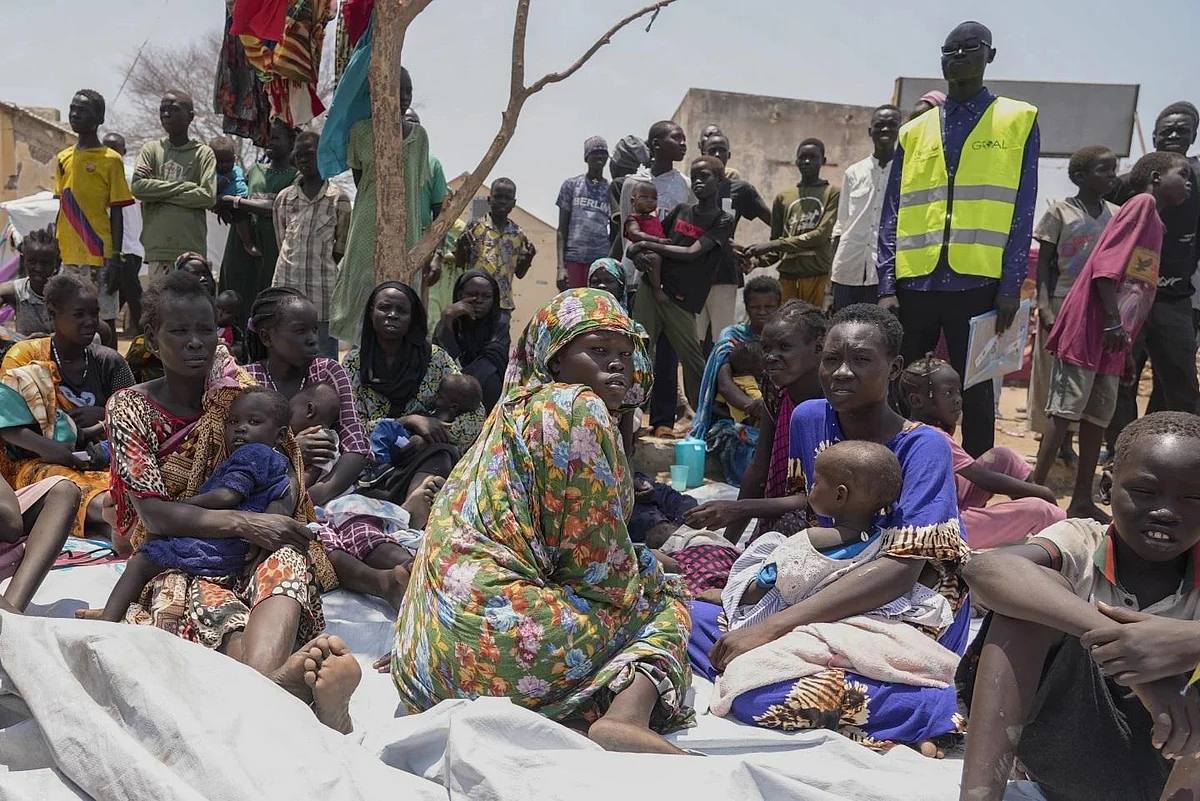 File photo of displaced women and children seated outdoors beside an aid worker in a hi-vis vest in South Sudan