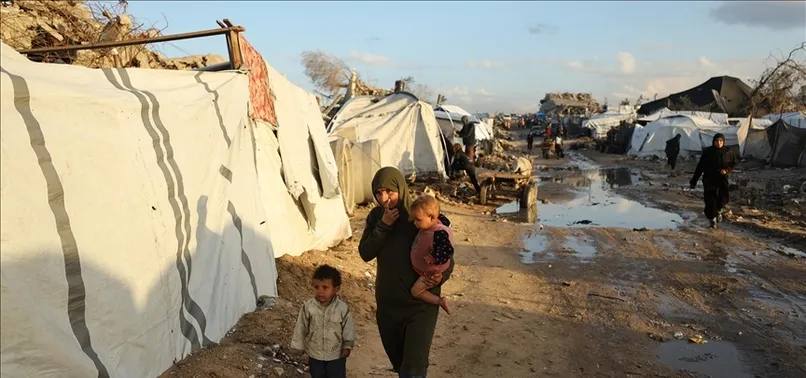 A Palestinian woman carrying a child walks past tents in a displacement camp in the West Bank