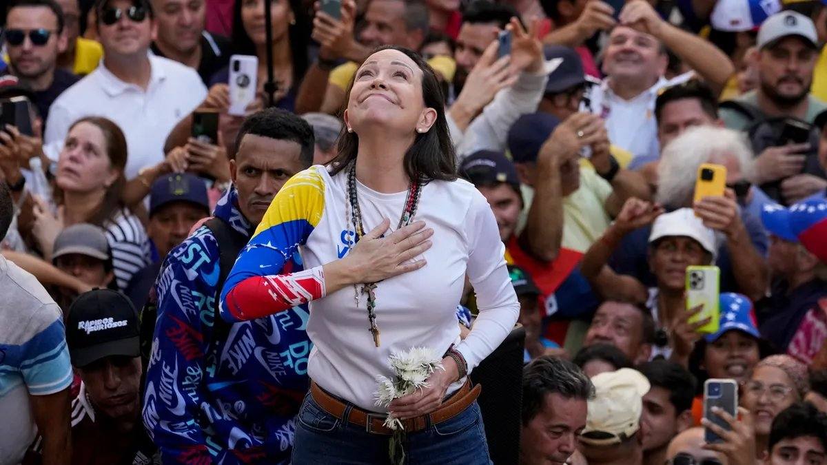 File photo of Venezuelan opposition leader Maria Corina Machado standing among supporters, hand on her heart, wearing a white top with Venezuelan flag colours on one sleeve