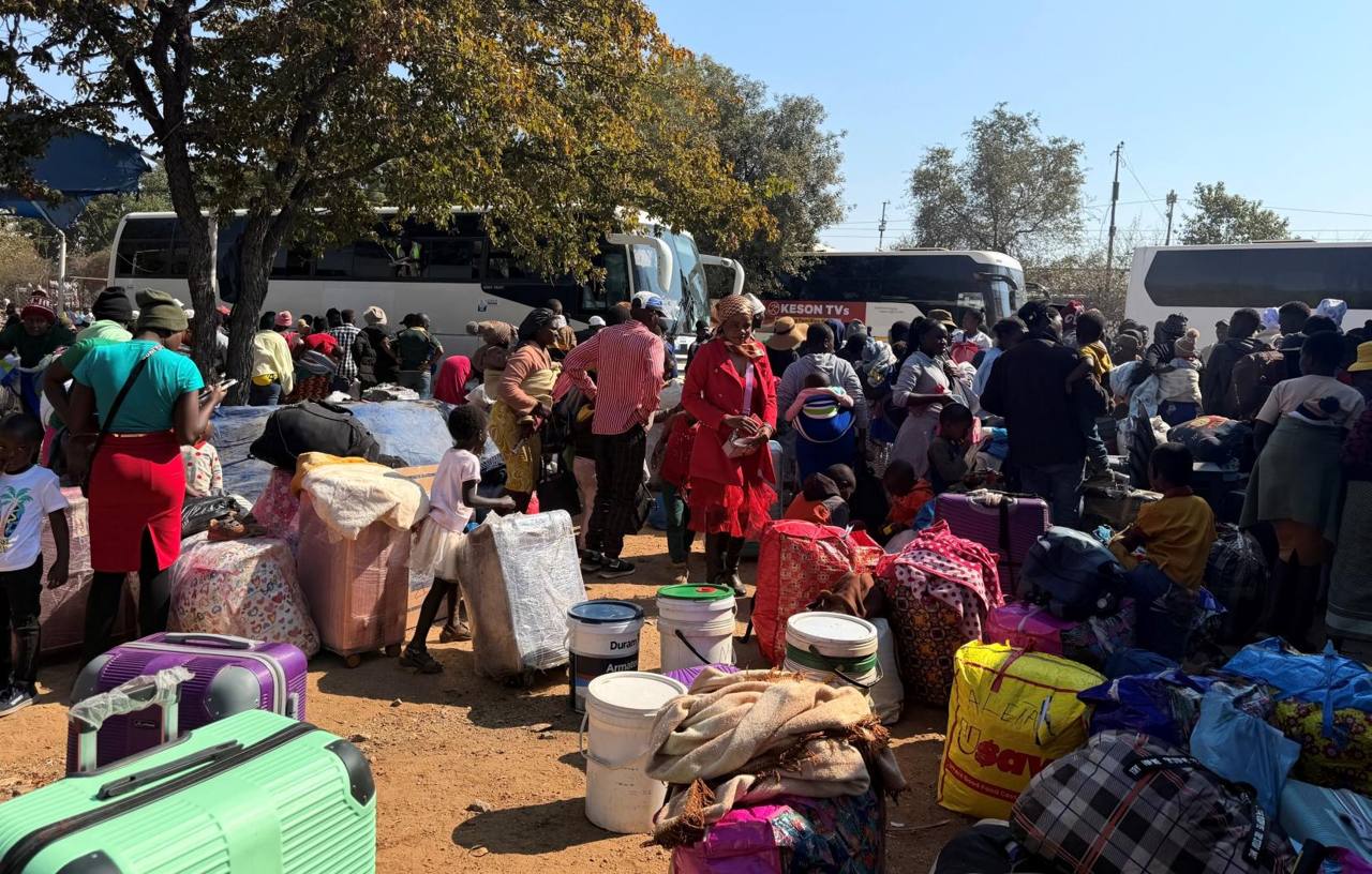 Zimbabwean returnees with suitcases, bags and buckets gathered beside buses at a reception point after returning from South Africa