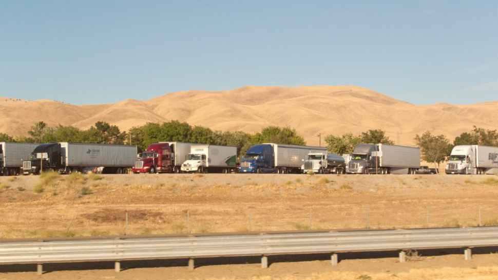 Semi trucks parked along Interstate 5 in California, with dry golden hills behind them