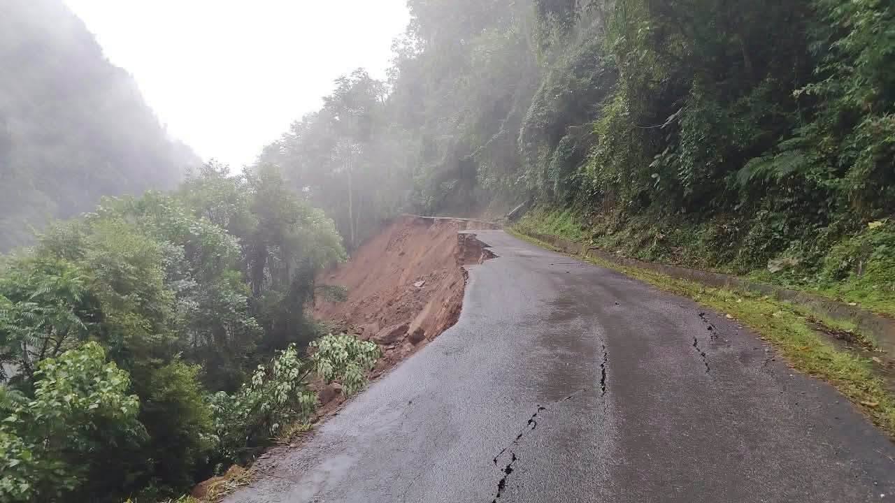 A mountain highway in Bhutan washed away by floodwater after the Shintaphu glacial lake outburst, with the road surface collapsed into a muddy slope above a forested valley