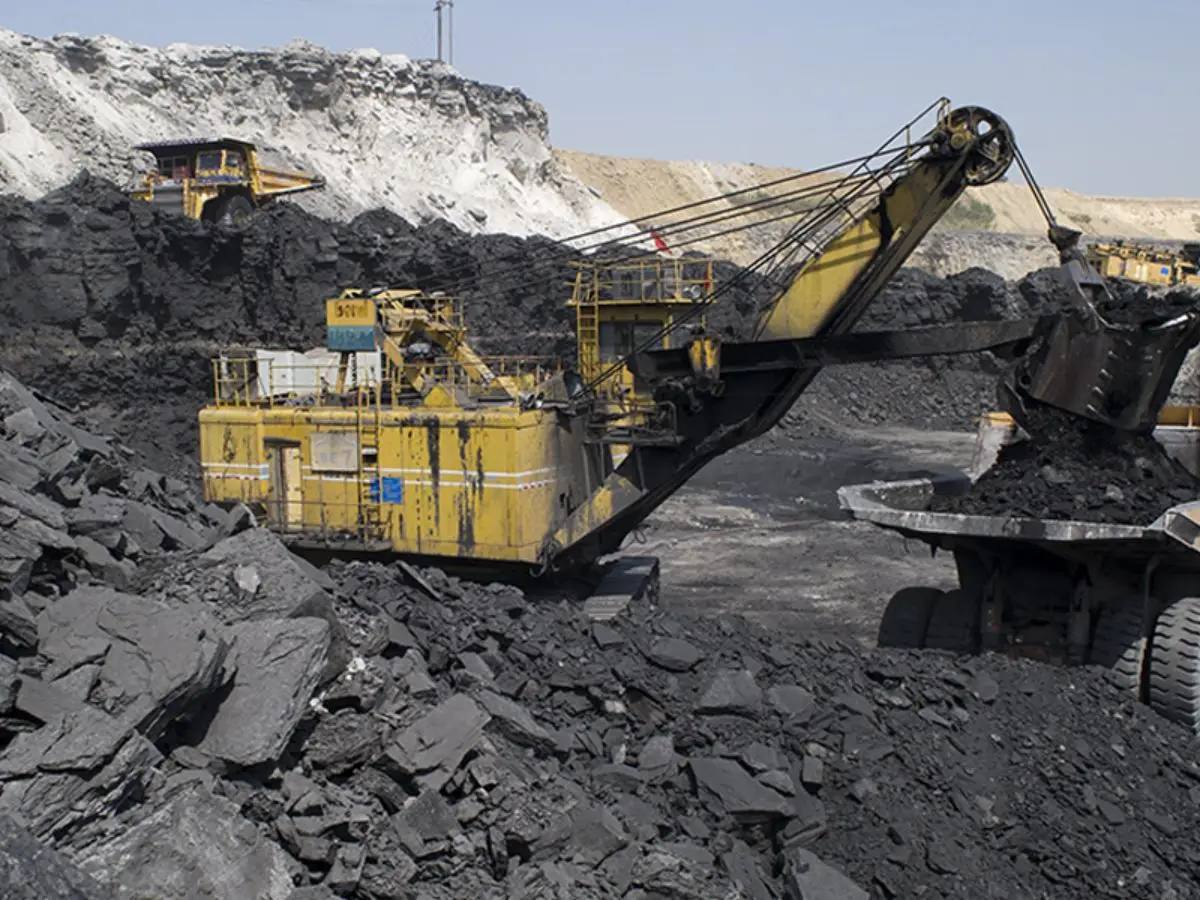A large yellow rope shovel loading coal into a dumper truck at an open-cast coal mine in India