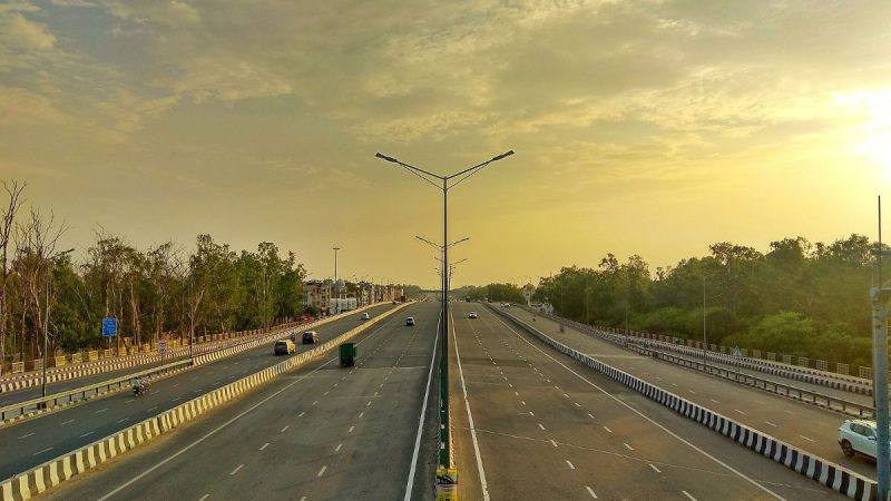 A completed multi-lane stretch of the Delhi-Mumbai Expressway at sunset, with a few vehicles on the road