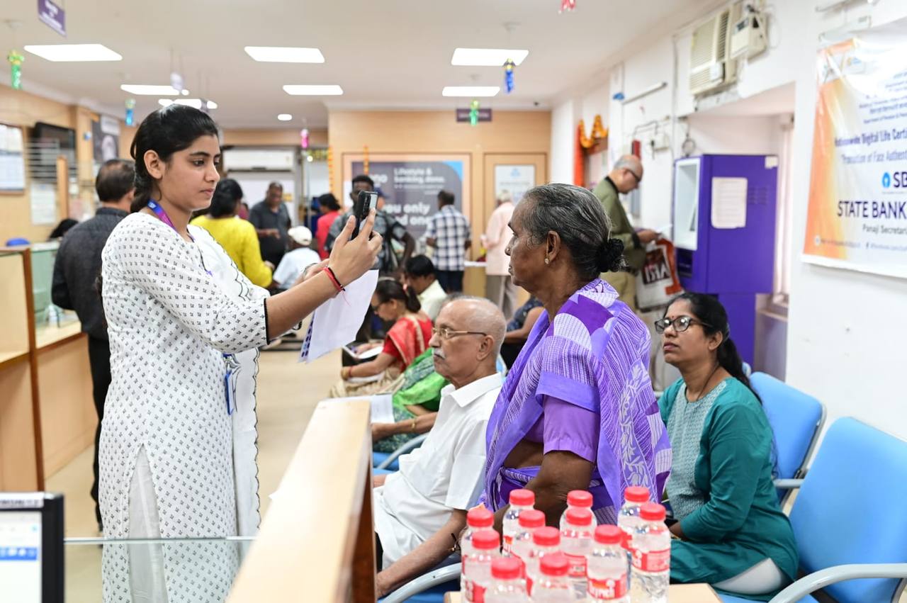 A pensioner completing face authentication on a smartphone held by a bank official at a Digital Life Certificate camp