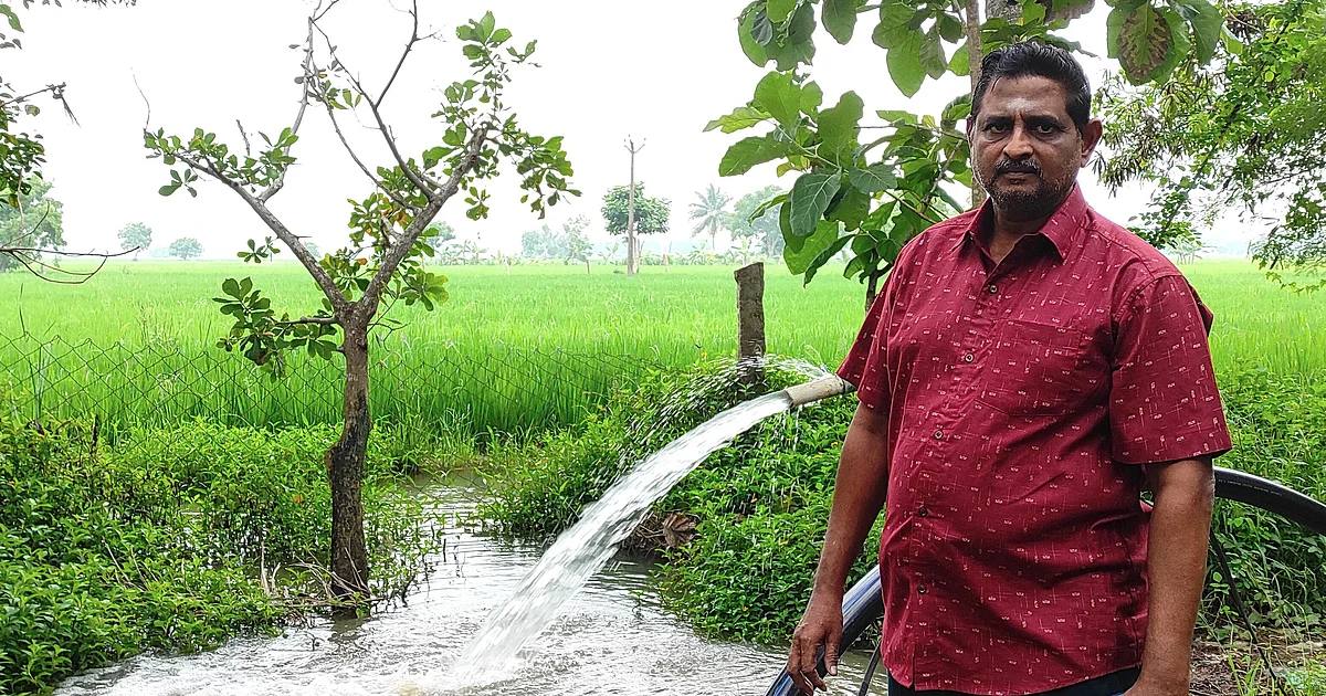 A farmer standing beside a running irrigation pump watering a green paddy field in Tamil Nadu