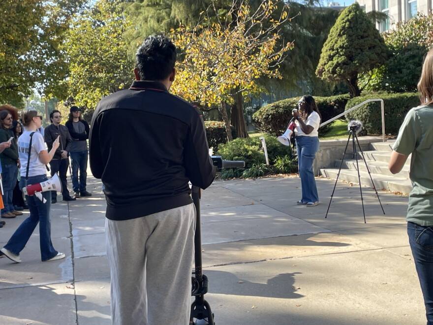 Pearl Essel speaking through a megaphone to supporters outside Carrington Hall at Missouri State University during a rally for her detained husband